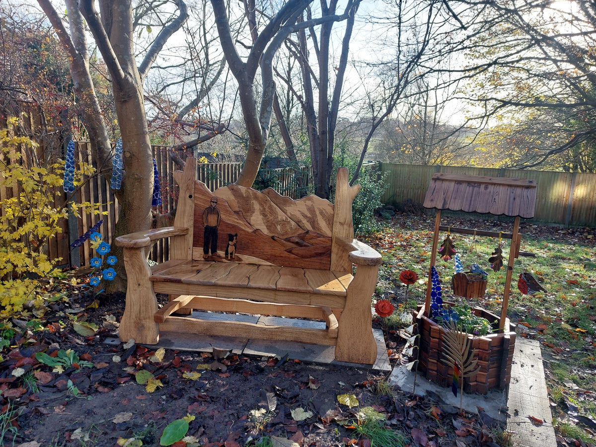 Three-seater solid oak garden bench with the Everest range carved in layered oak across the backrest, in a garden under a magnolia