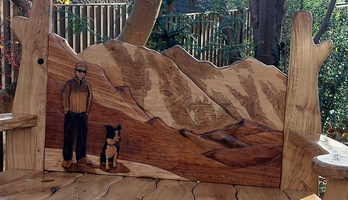 Close-up of the layered oak backrest: Everest and Lhotse in stained oak with a carved figure and collie in the foreground