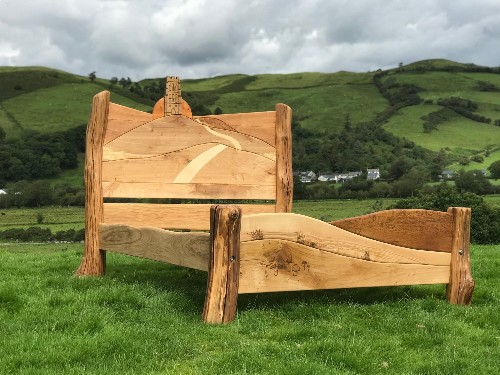 Side view of Glastonbury Tor sunrise carved bed — handcrafted bespoke oak bedroom furniture, Wales