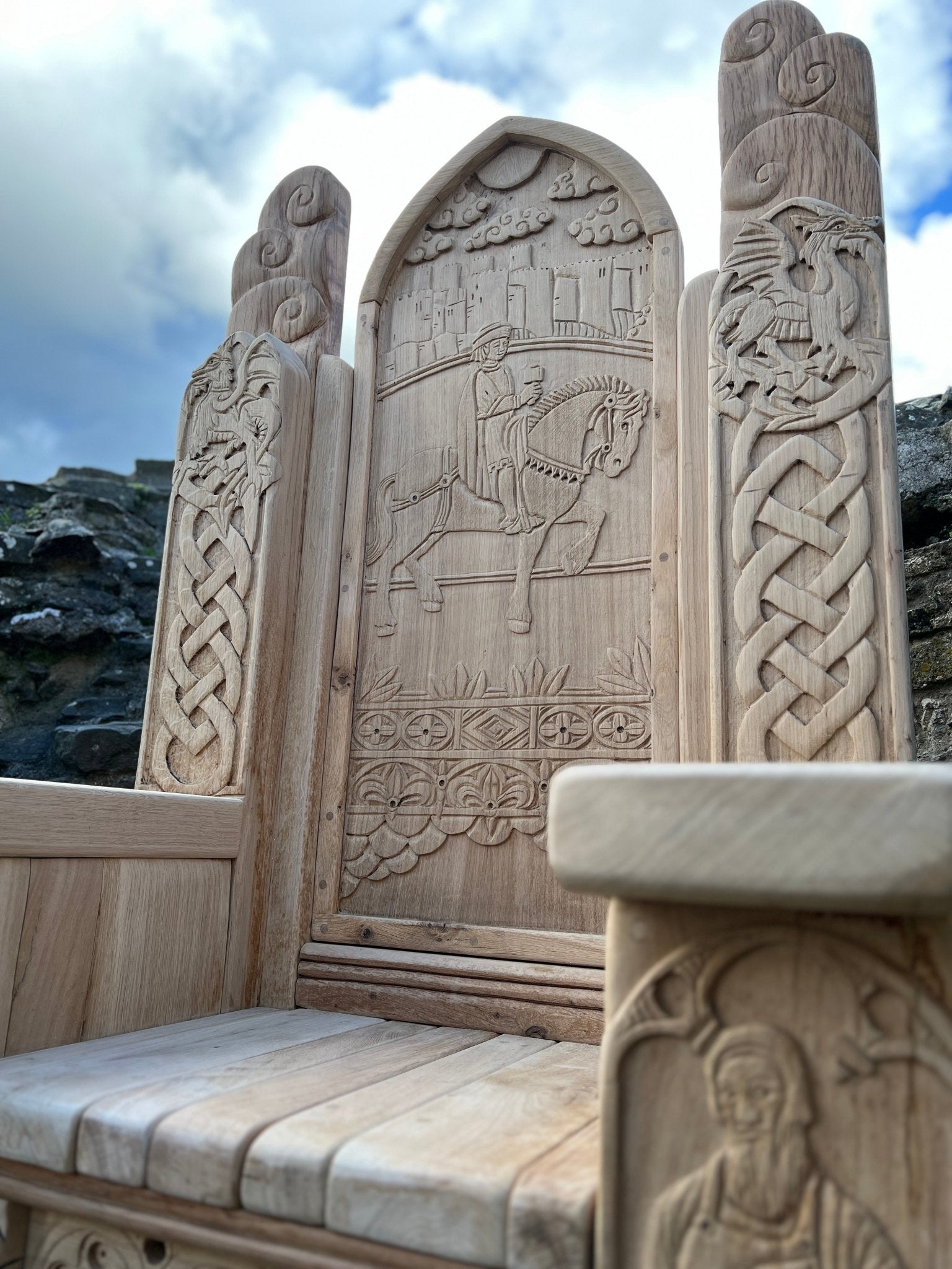Close-up view of intricate hand-carved details on an oak throne at Conwy Castle, featuring Celtic knots, a knight on horseback, and mythical designs.