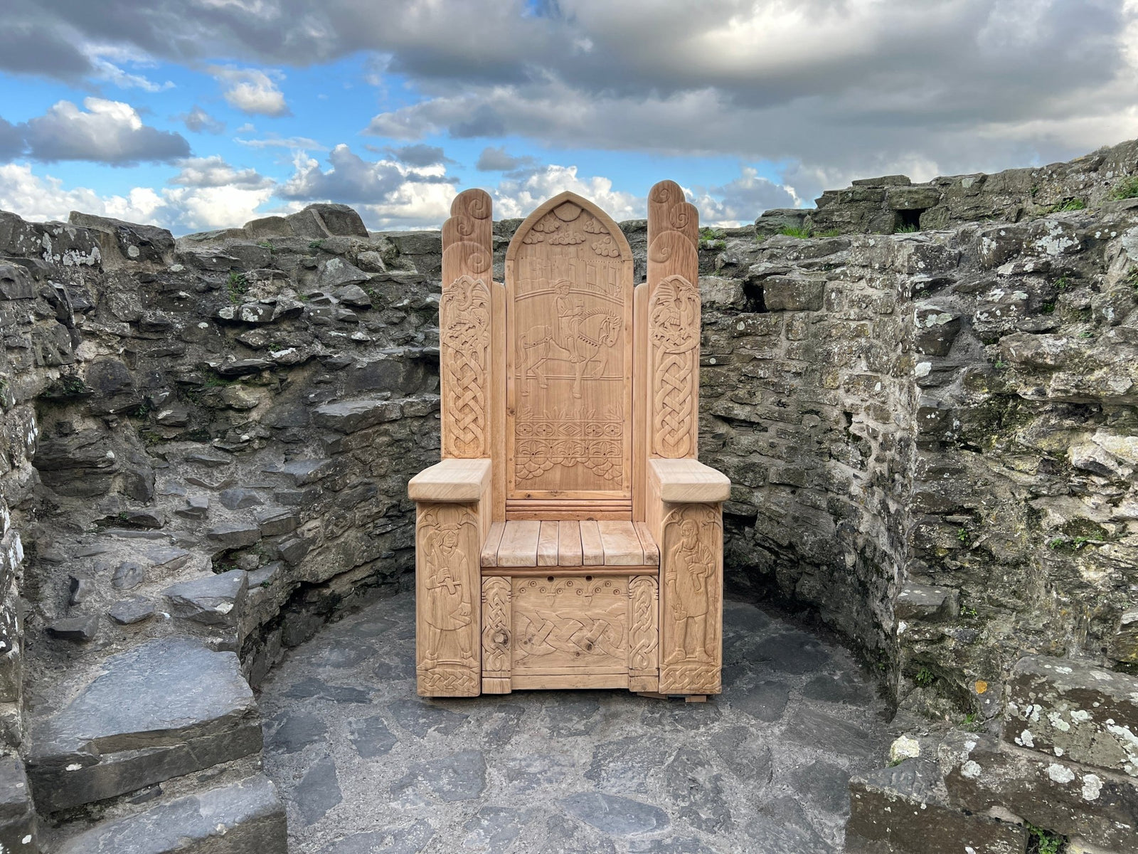Hand-carved oak throne featuring intricate Celtic and historical carvings, displayed within the stone walls of Conwy Castle in North Wales