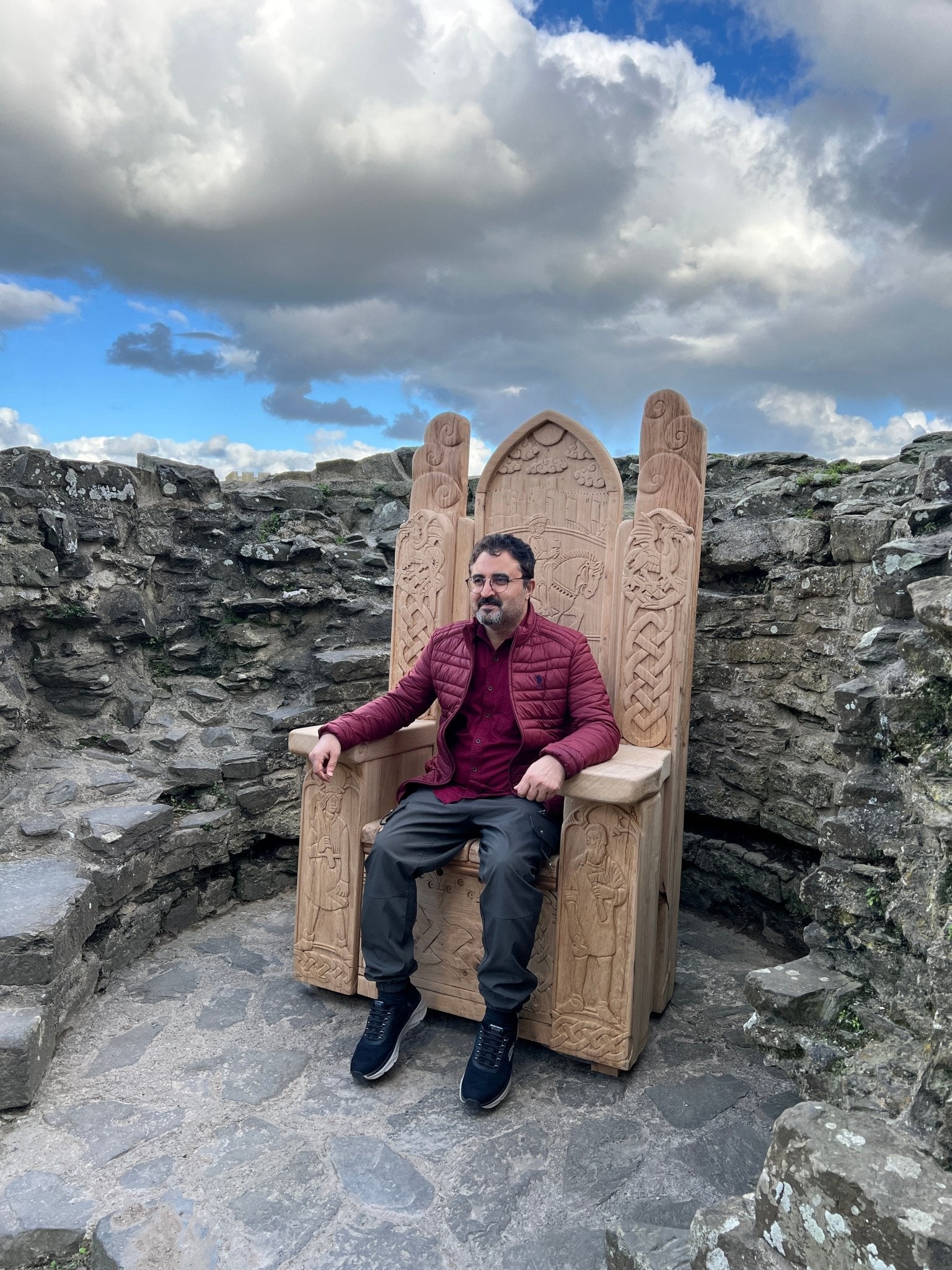 A visitor seated on a hand-carved oak throne with intricate Celtic designs and historical carvings, displayed at Conwy Castle in North Wales.