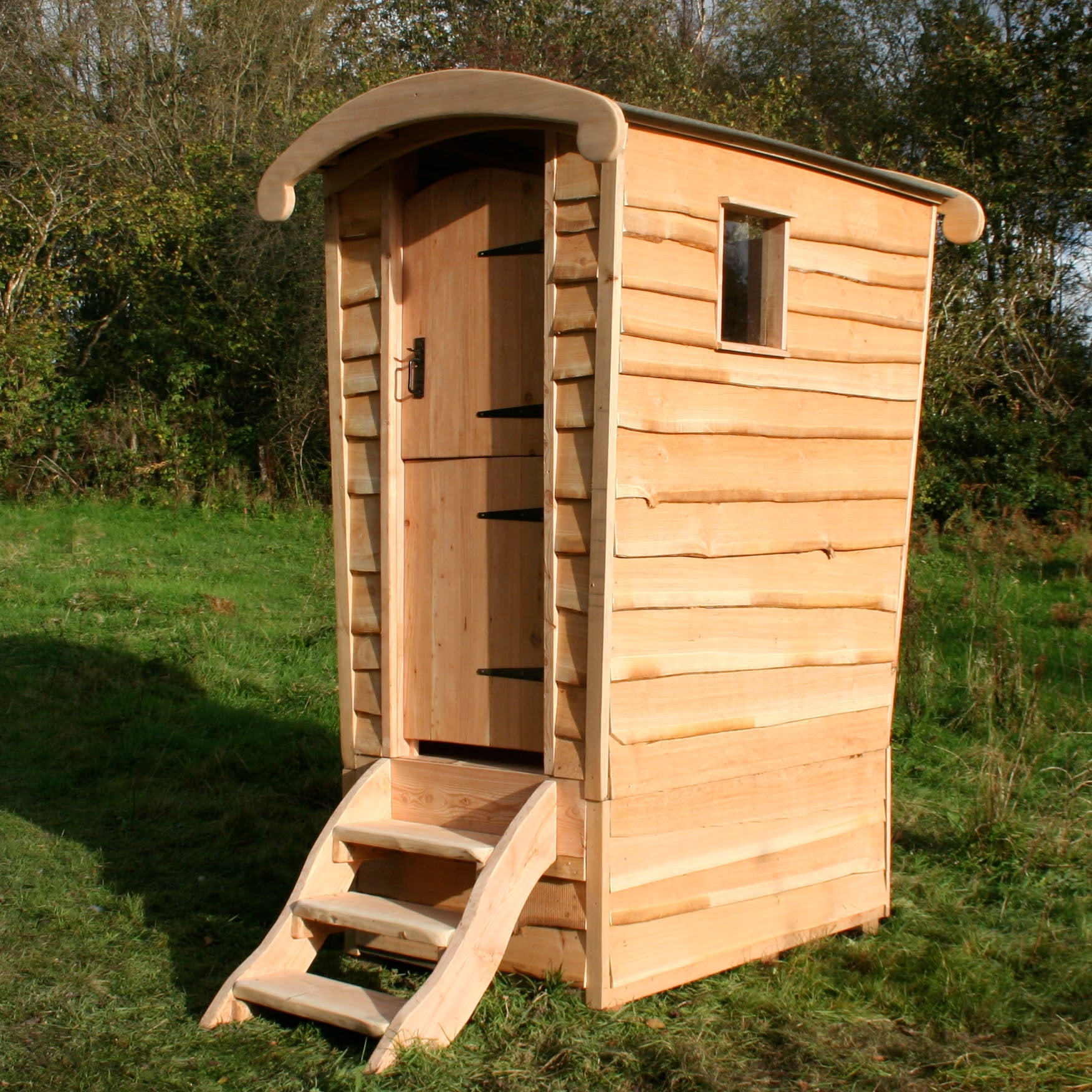 Toilettes à compost écologiques fabriquées à la main par Free Range Designs, avec une structure rustique en bois, un toit incurvé et un revêtement naturel, s'intégrant parfaitement aux environnements extérieurs pour une solution durable et élégante.