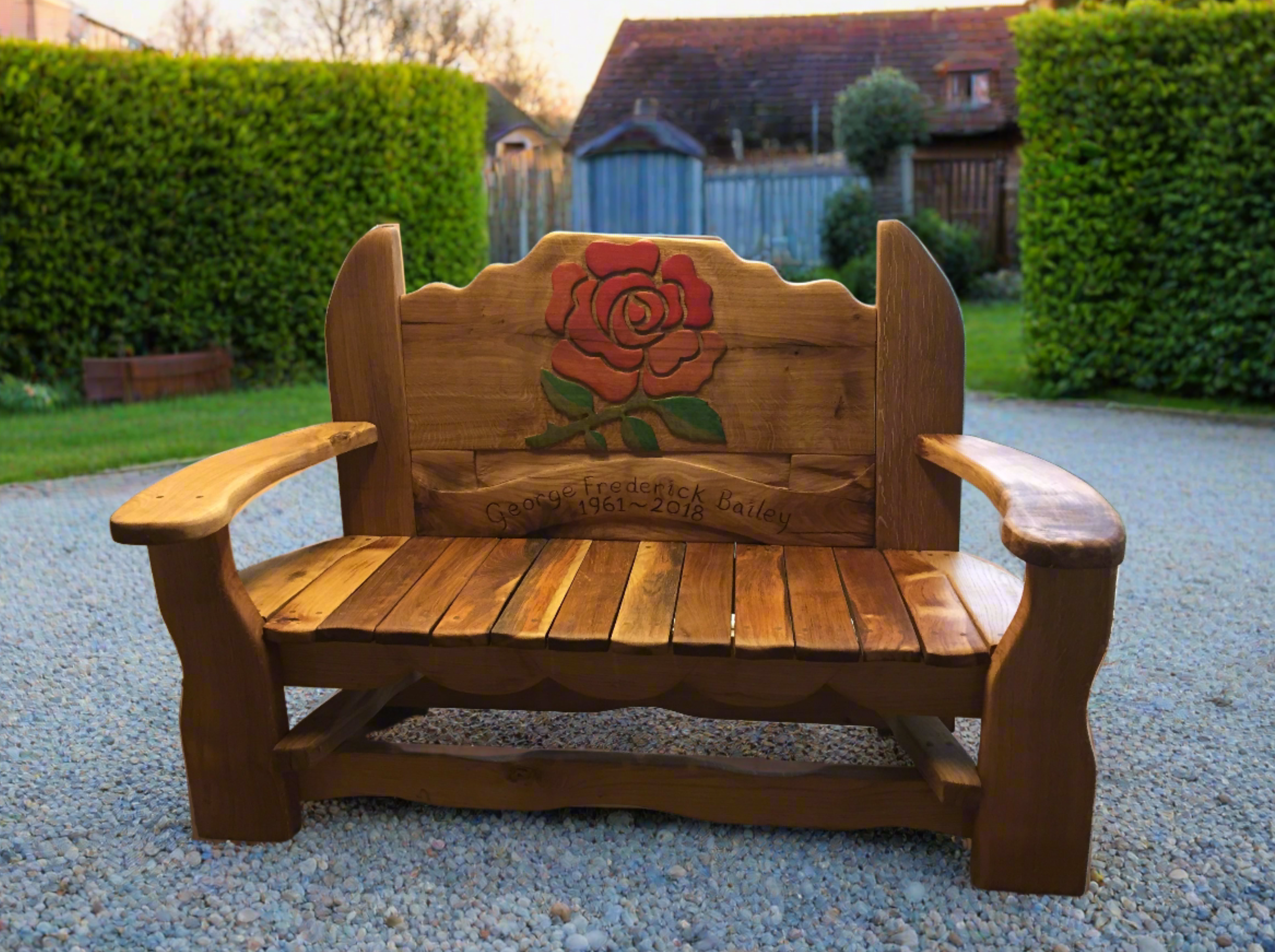 A handcrafted wooden memorial bench with a rose carving and personalized engraving reading "In Loving Memory of George Frederick Bailey, 1961-2018," designed for gardens or outdoor remembrance.

