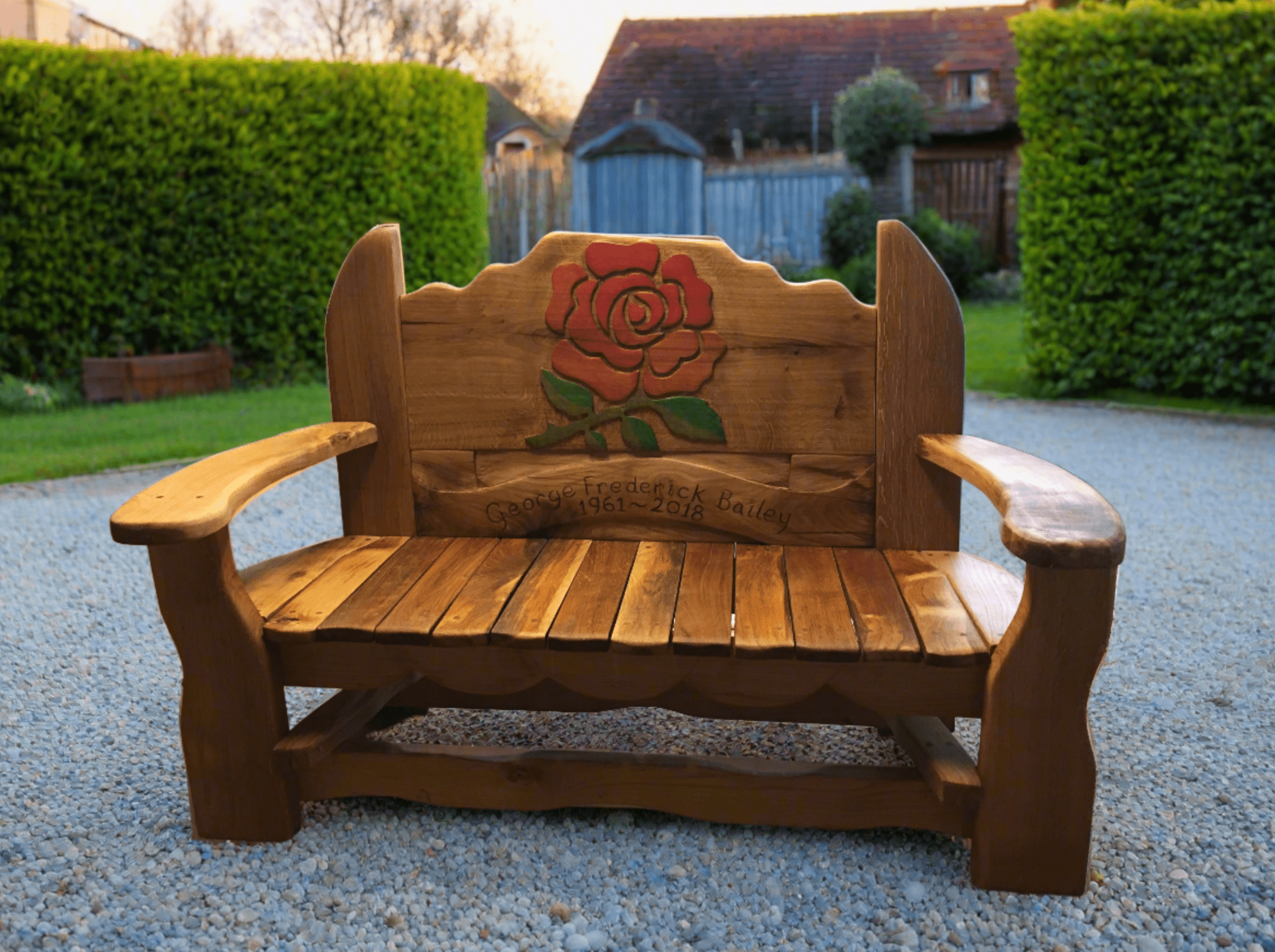 A handcrafted wooden memorial bench with a rose carving and personalized engraving reading "In Loving Memory of George Frederick Bailey, 1961-2018," designed for gardens or outdoor remembrance.

