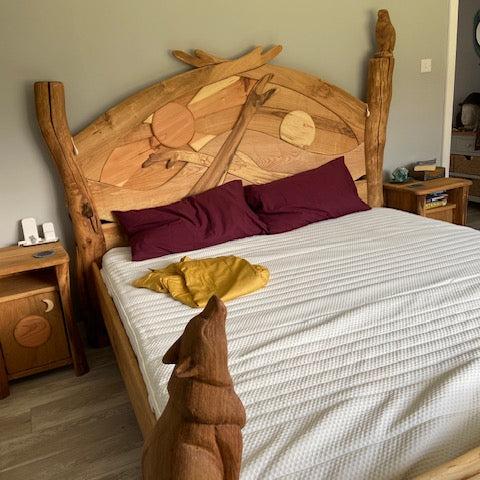 Handcrafted wooden sunrise bed with carved headboard featuring sun and tree motifs, complemented by matching night tables for a rustic bedroom design.