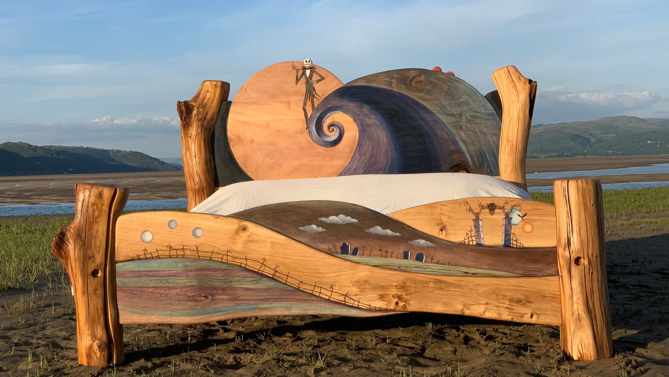 Handcrafted wooden bed featuring a whimsical 'Nightmare Before Christmas' inspired design, with unique carved details on the headboard and footboard depicting a swirling night sky and dreamlike landscapes, set against a stunning natural backdrop