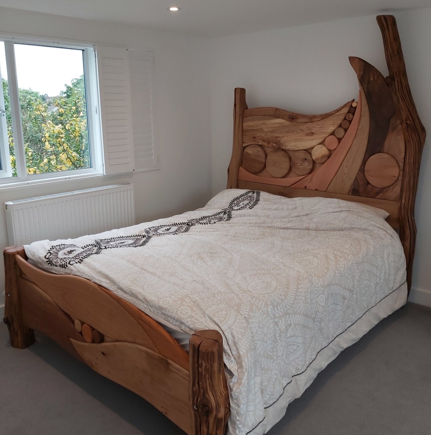 Handcrafted wooden bed frame with unique constellation design headboard, showcasing natural wood grains and circular accents, placed in a bright, minimalist bedroom