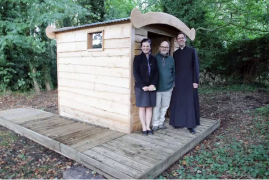 Three people standing beside a wooden compost toilet