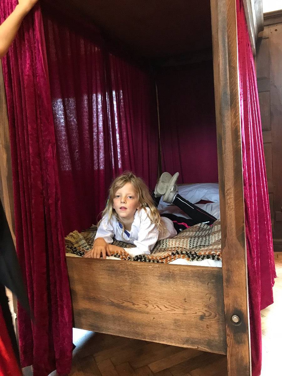 Child on a wooden canopy bed with red curtains