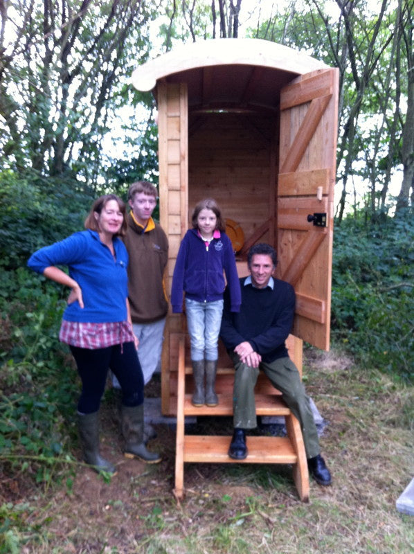 Family posing by wooden composting toilet in forest