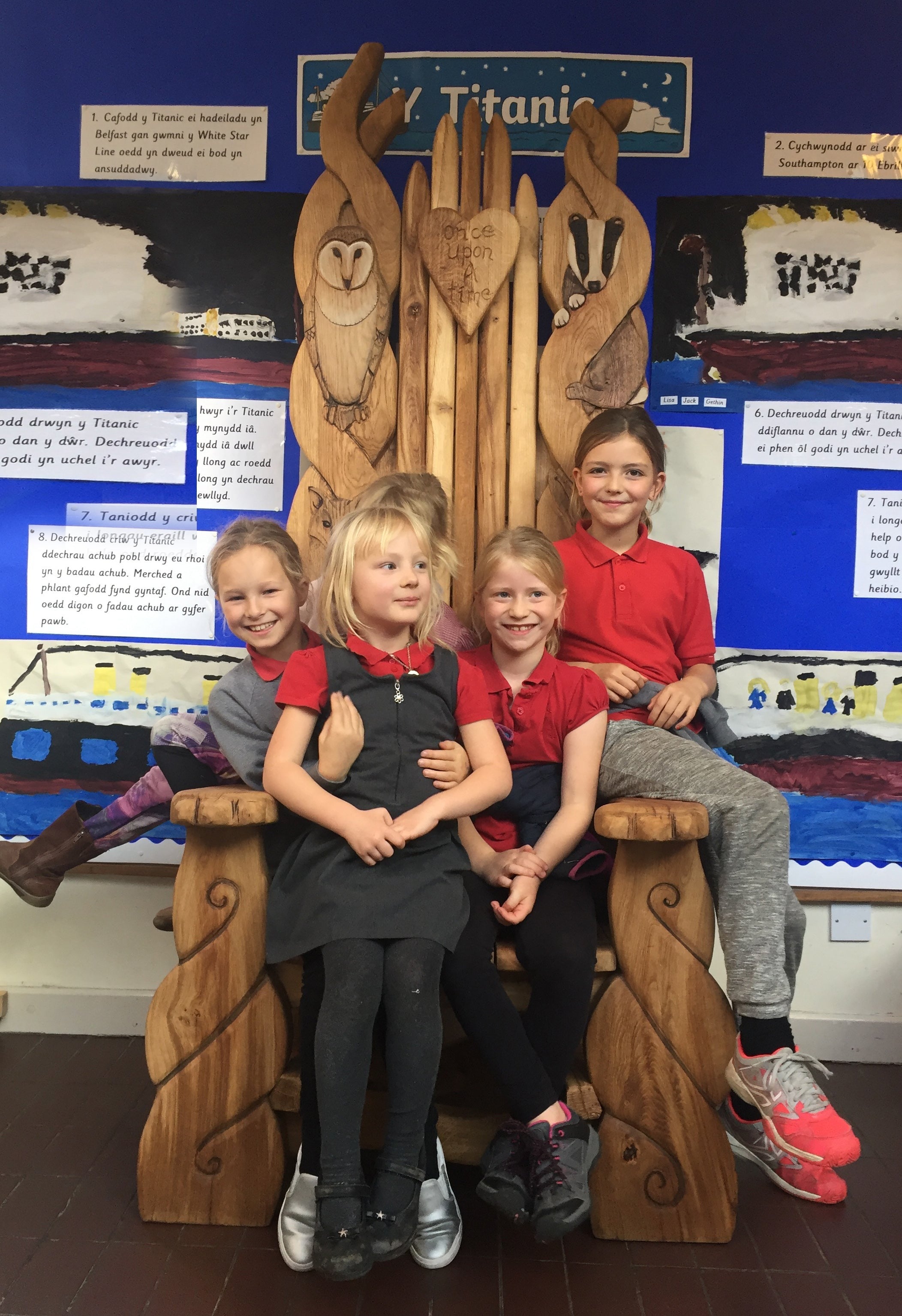 Groupe d'enfants sur une grande chaise en bois avec des sculptures d'animaux.