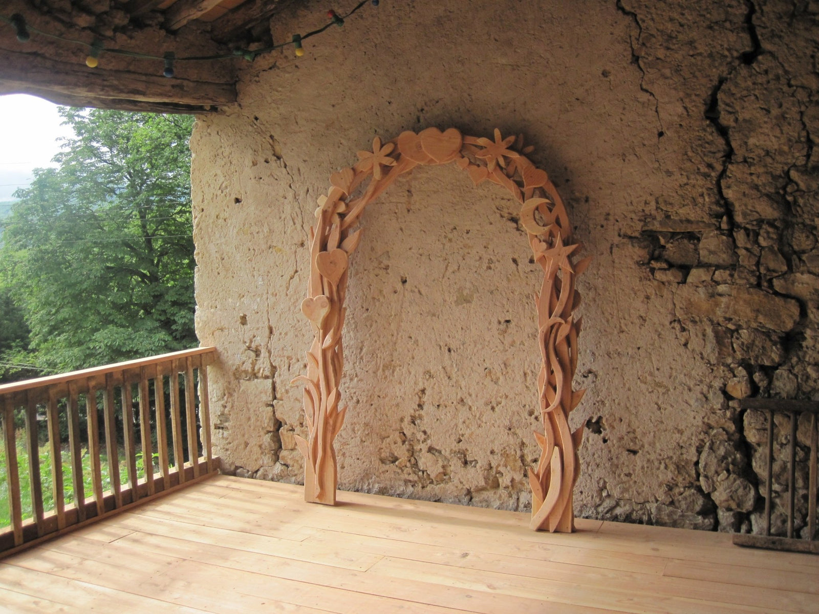 Wooden arch with floral design against a stone wall on a wooden deck.