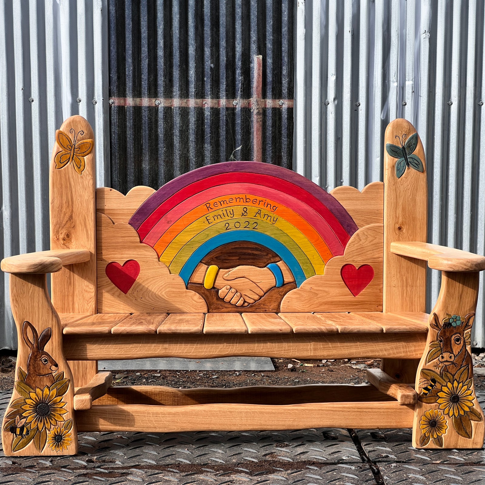 Hand-carved solid oak memorial garden bench with rainbow centrepiece, clasped hands and butterfly finials | front view