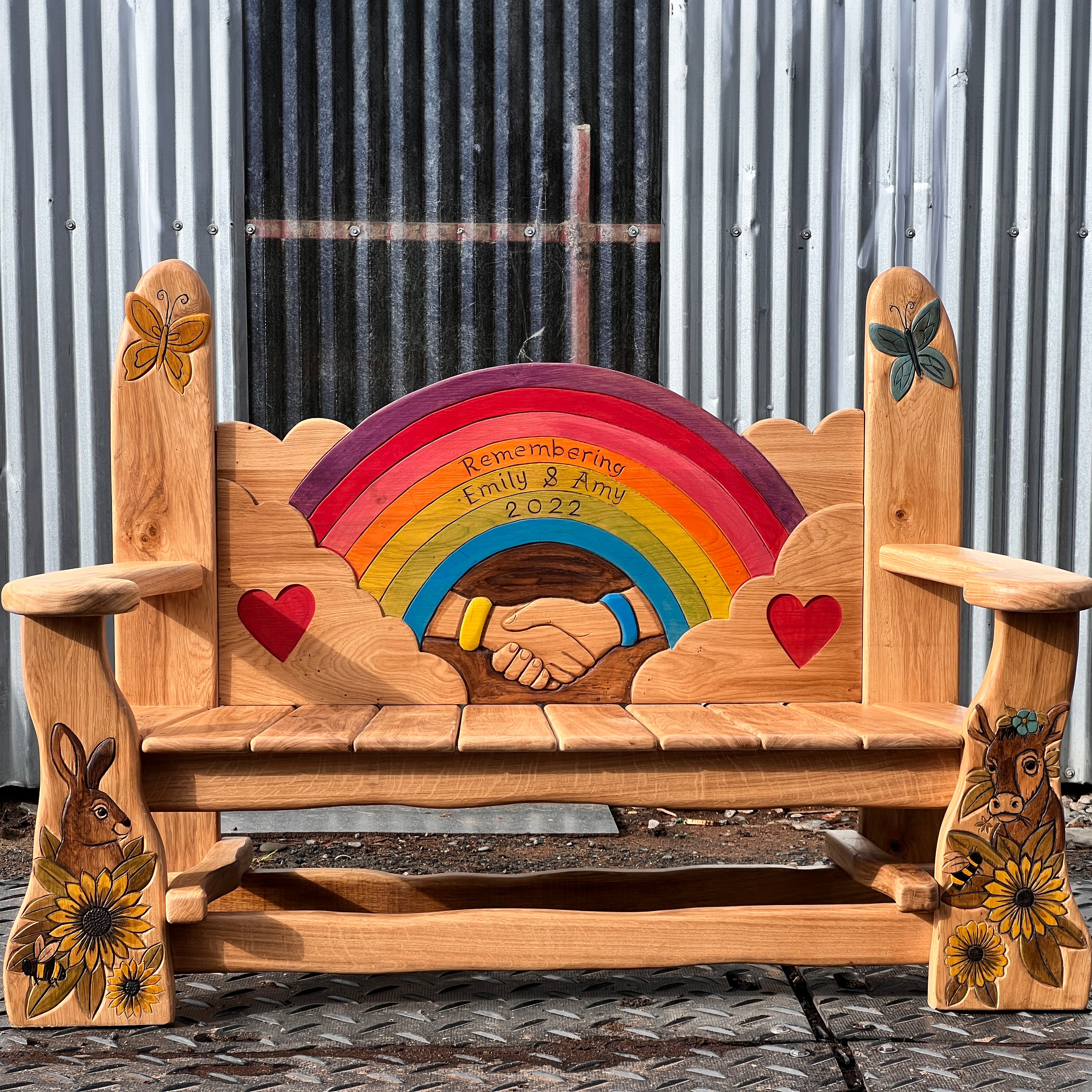 Hand-carved solid oak memorial garden bench with rainbow centrepiece, clasped hands and butterfly finials | front view