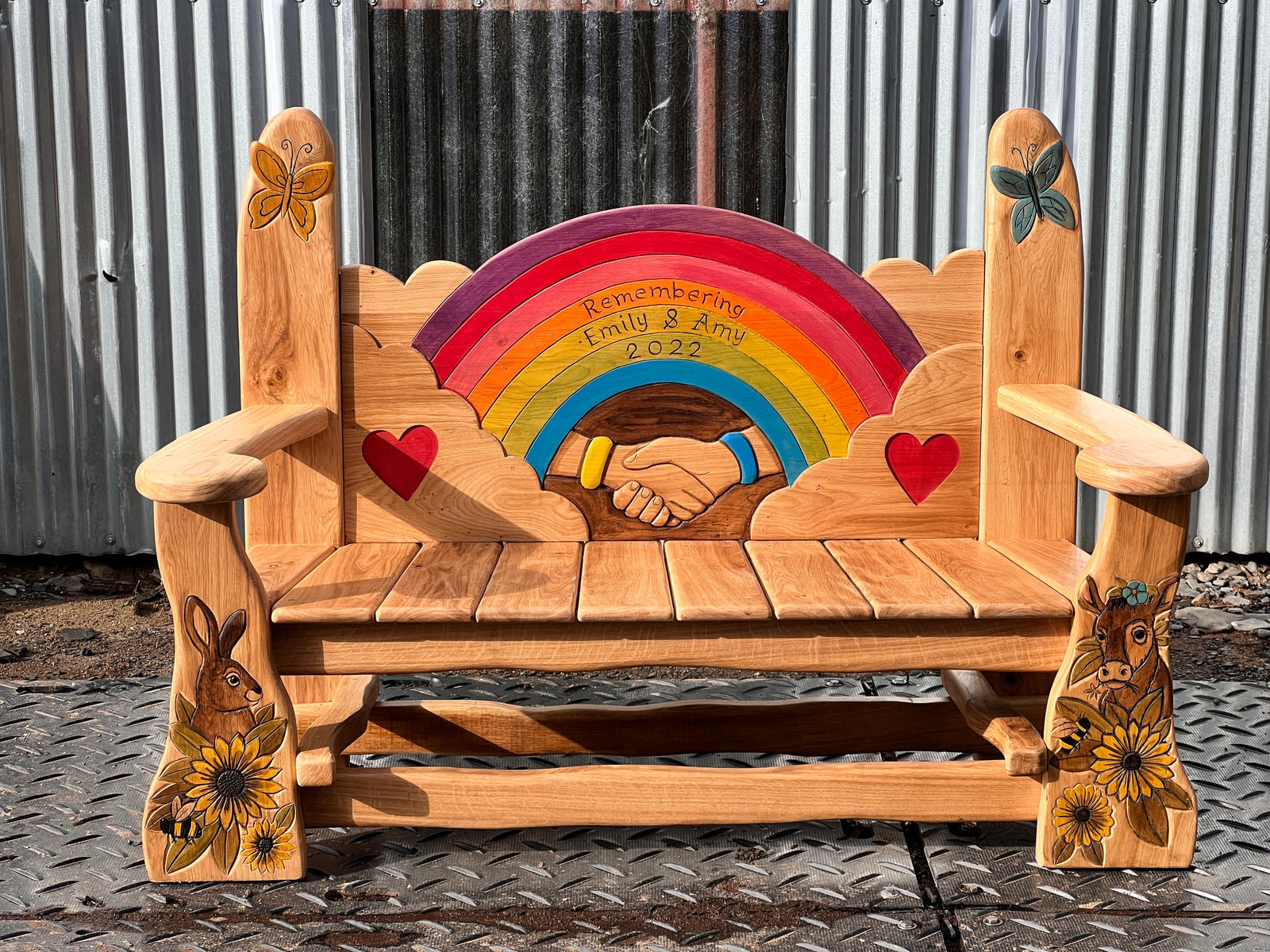 Hand-carved oak memorial garden bench side angle showing scalloped backrest, armrests and carved leg details
