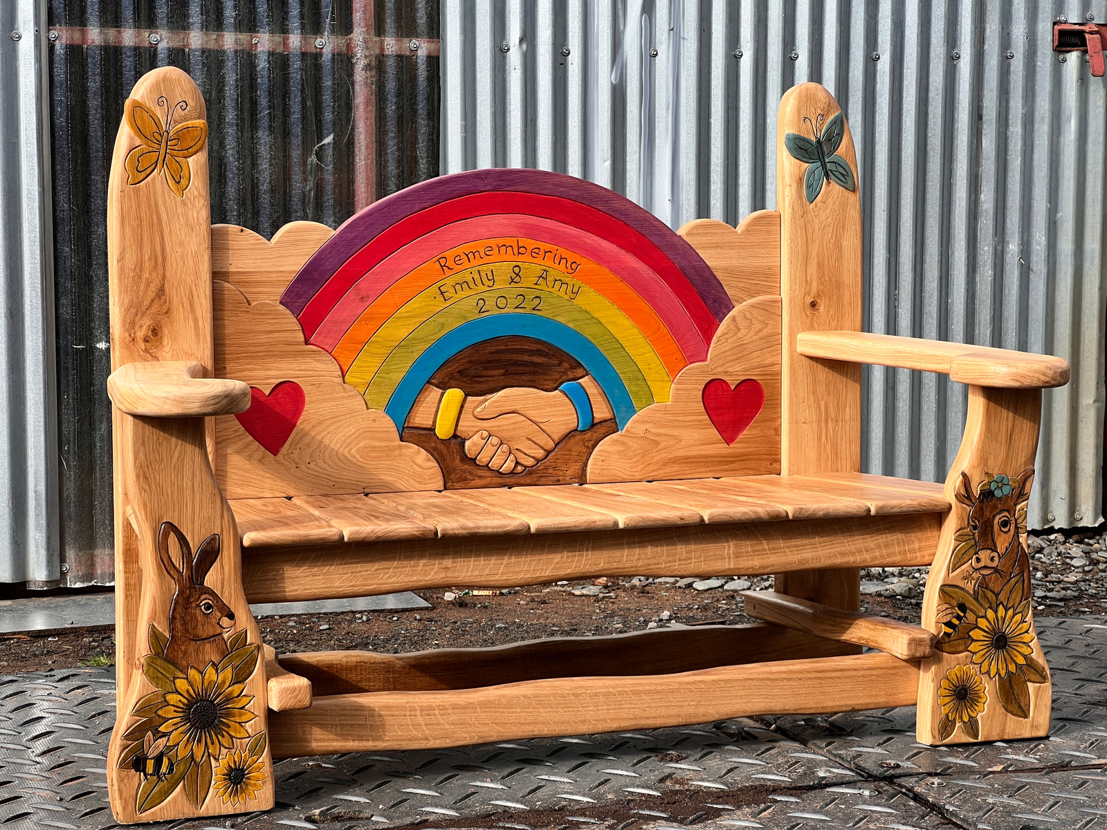 Solid oak memorial bench angled view showing carved hare with sunflowers and highland cow on front legs