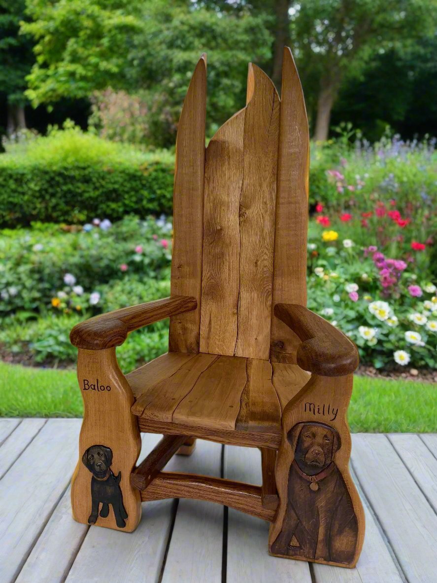 A handcrafted memorial wooden chair with detailed dog carvings of Baloo and Milly, placed on a wooden deck with a vibrant garden in the background, symbolizing remembrance and artistic craftsmanship.