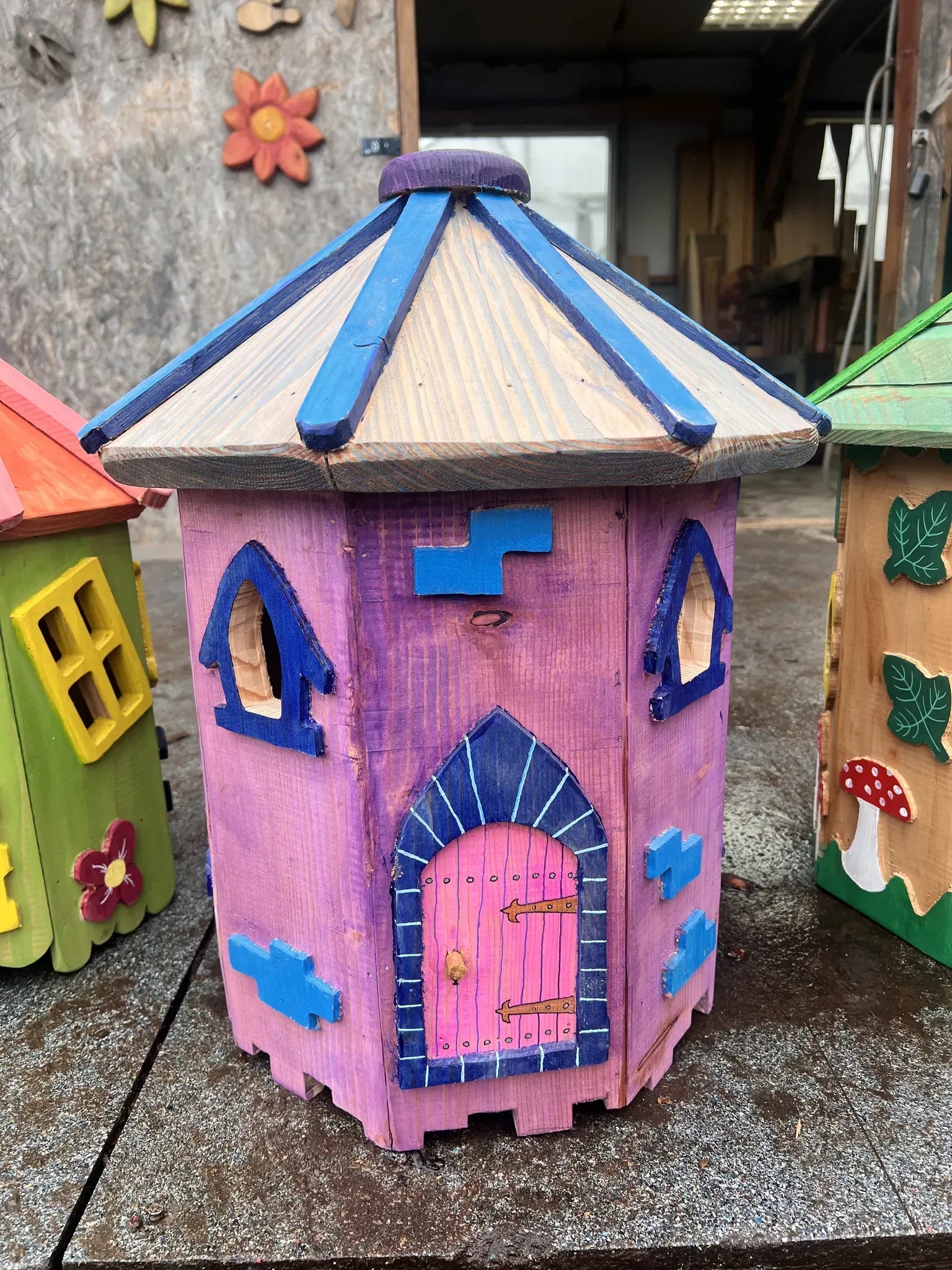 Angle view of small hexagonal fairy cottage showing painted window details and reclaimed wood walls
