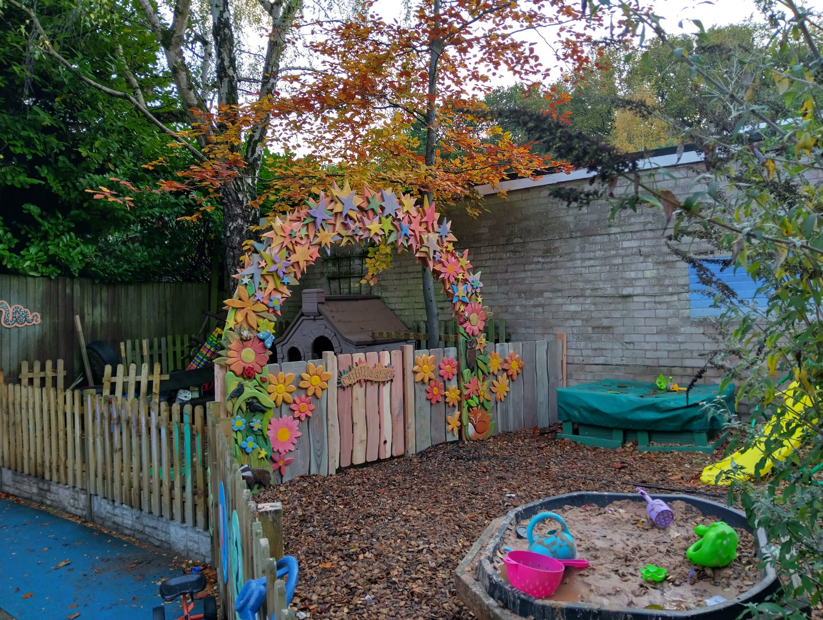 Children's play area with a colorful flower arch, sand pit, and toy house.