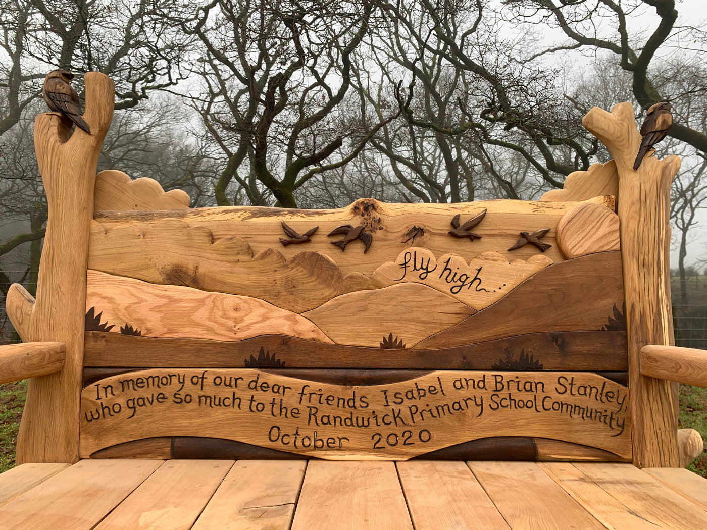 Memorial bench with landscape carving and dedication text.