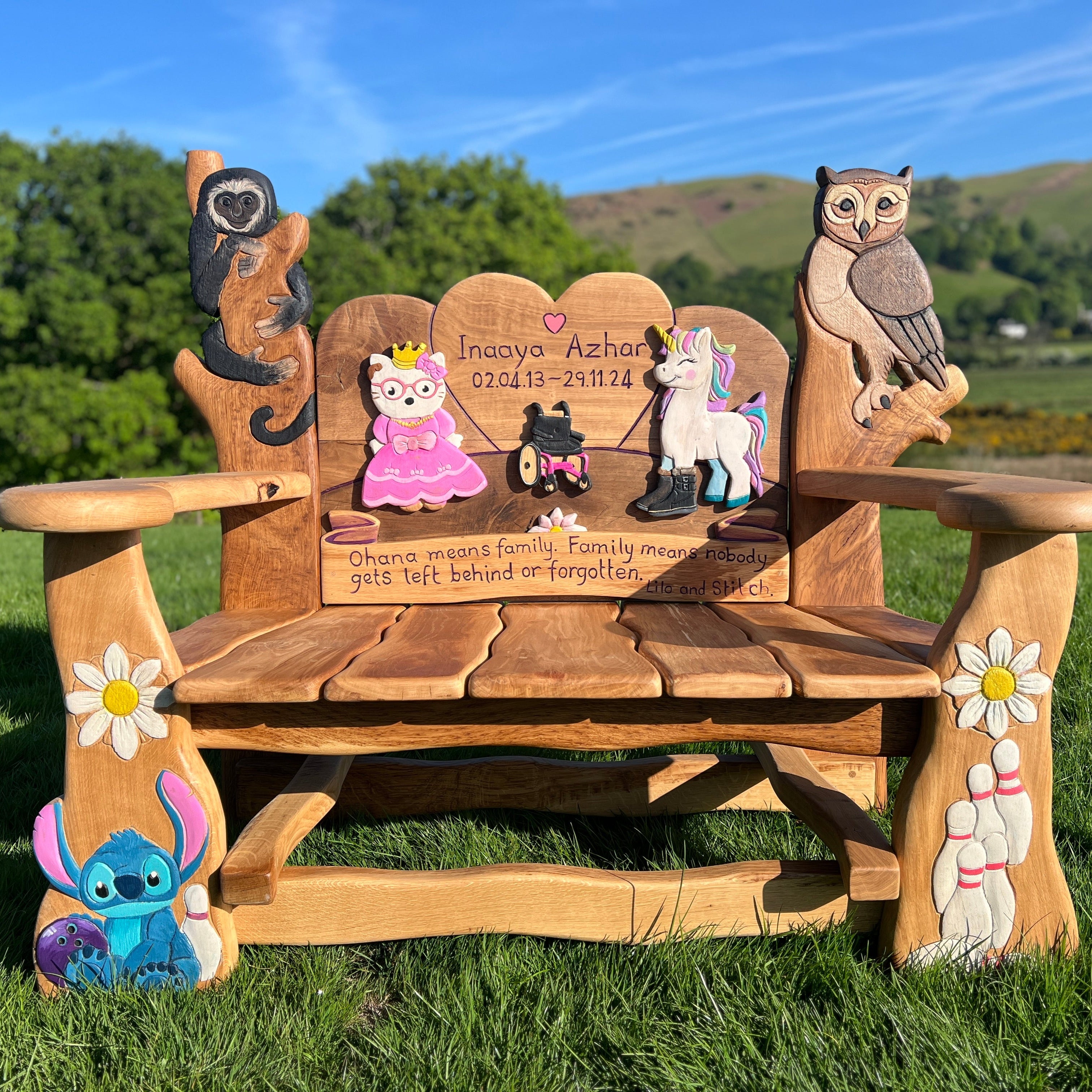 Handcrafted children’s memorial bench with carved and painted characters including Stitch, an owl, a unicorn, and a princess, with engraved dedication text.