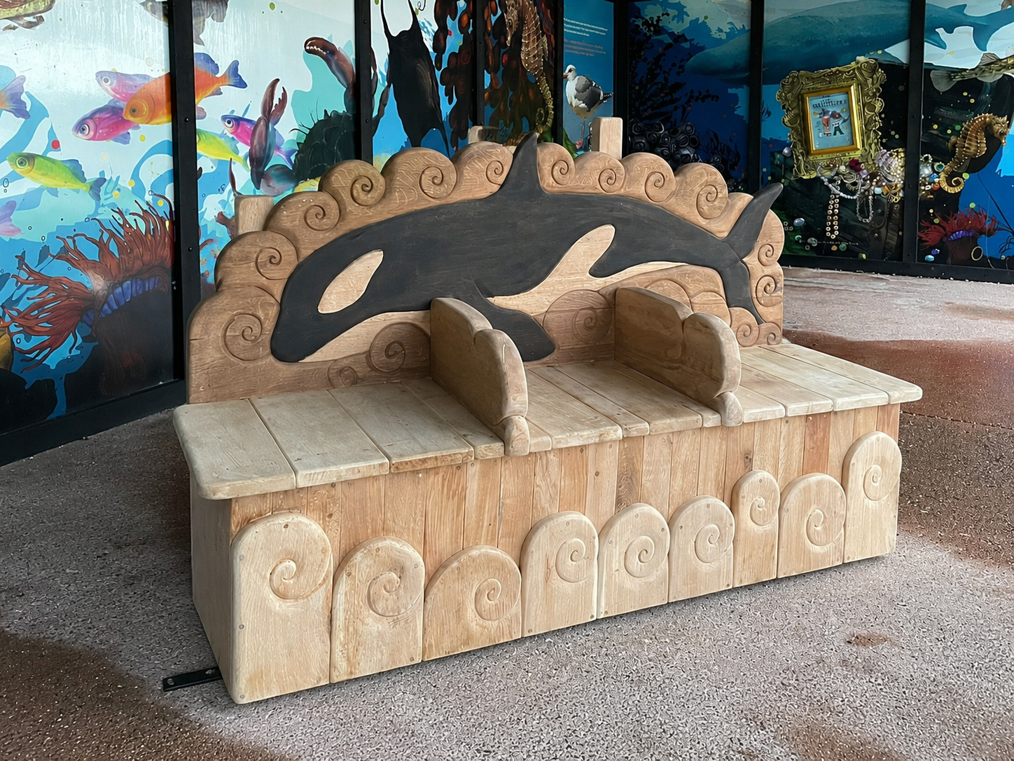 Orca bench side angle showing DDA-compliant armrests and hand-carved wave details in solid oak