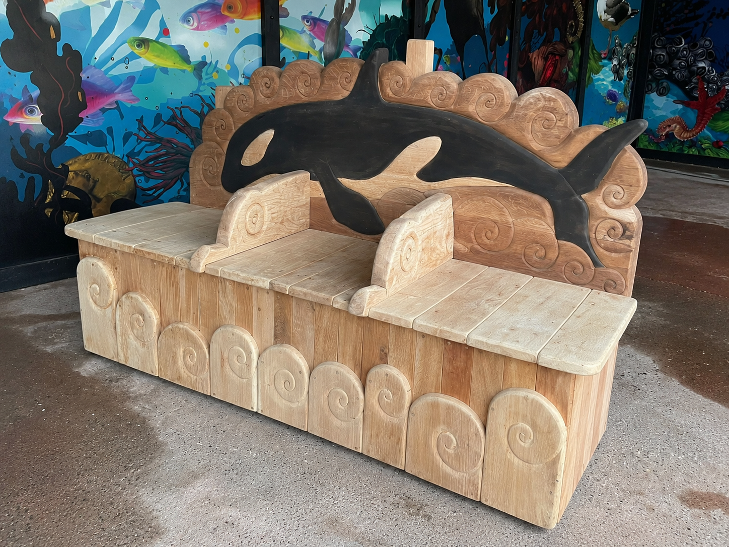 Three-quarter view of hand-carved oak orca bench showing wave base and orca leaping across backrest