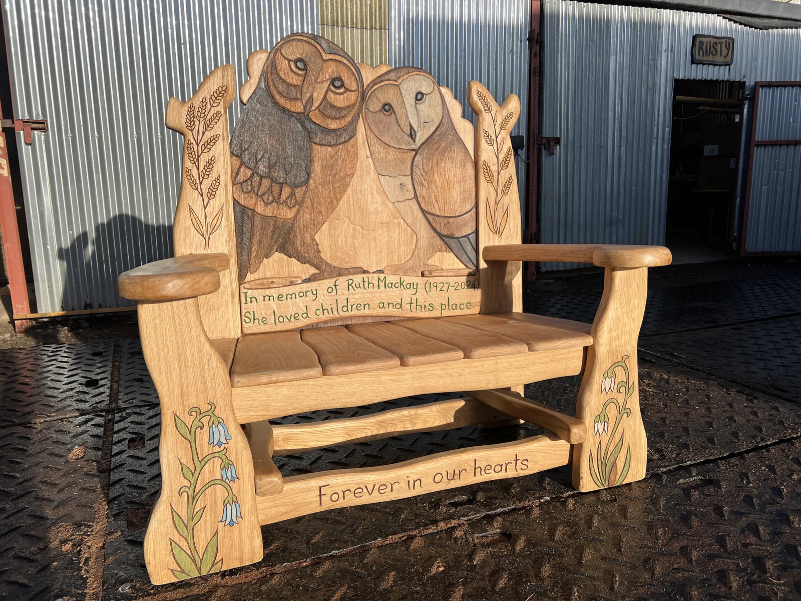 Full view of bespoke hand-carved oak memorial bench with painted owls, bluebell carvings and personalised inscriptions