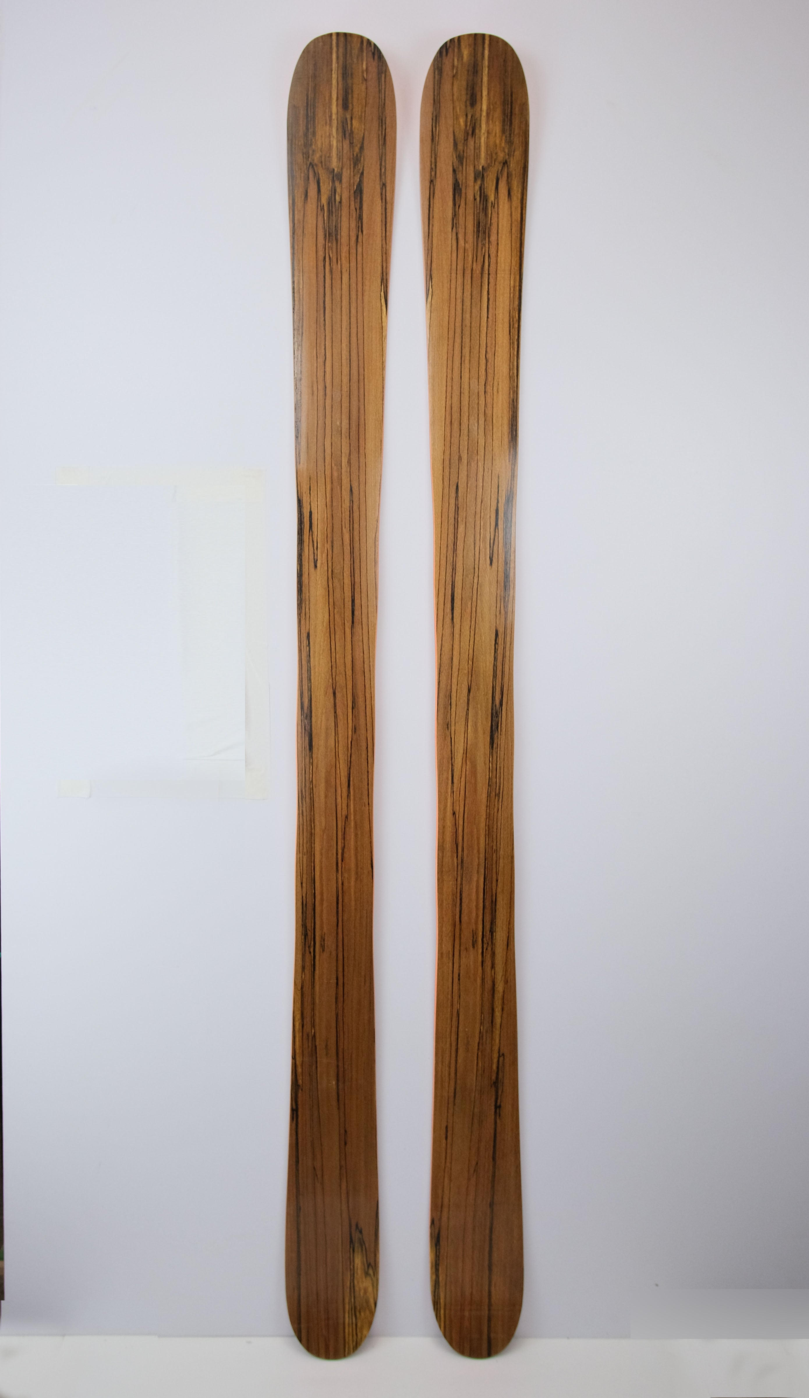 Front view of handmade Powder Playfull 117 skis with a spalted beech topsheet, vibrant orange sidewalls, and a natural wood finish, displayed upright against a white backdrop.