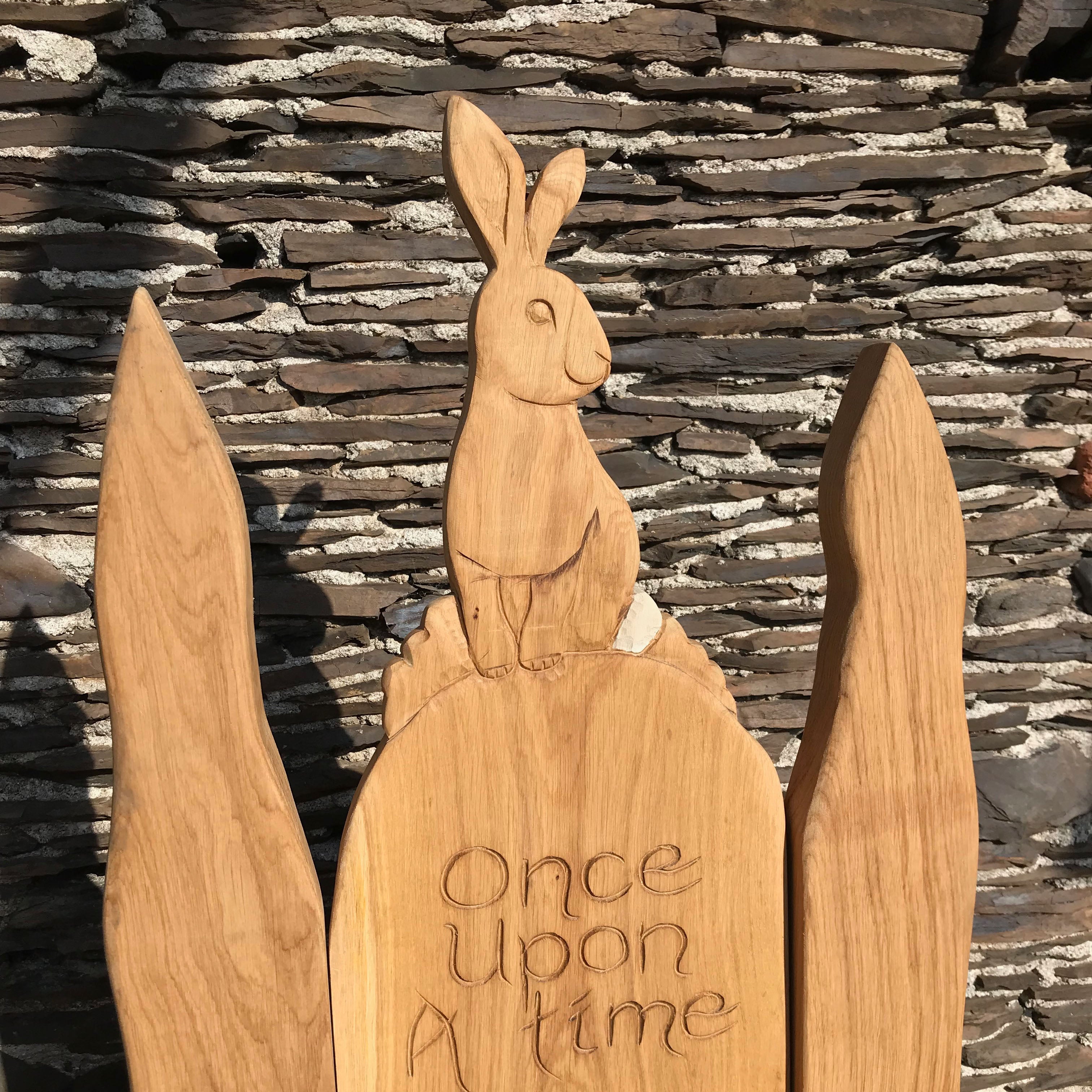 Rabbit carving on wooden chair with stone wall background.