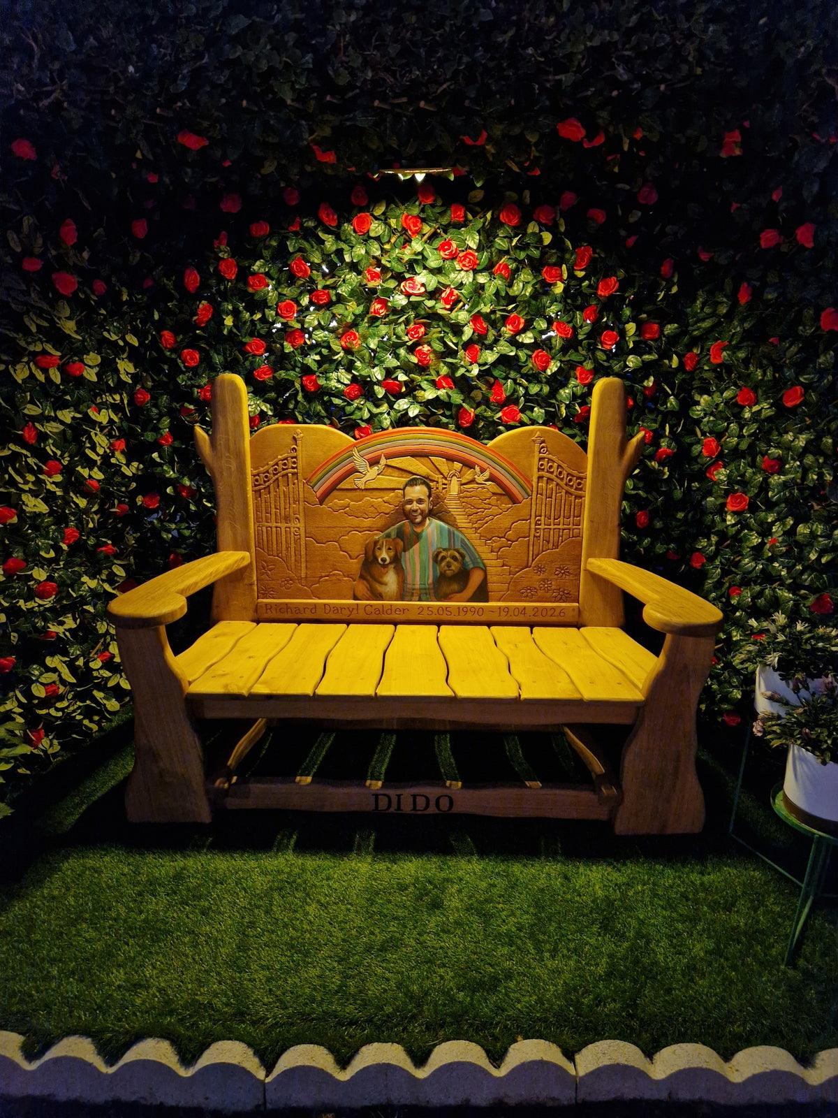 Painted portrait memorial bench in carved oak lit at dusk under a rose arbour