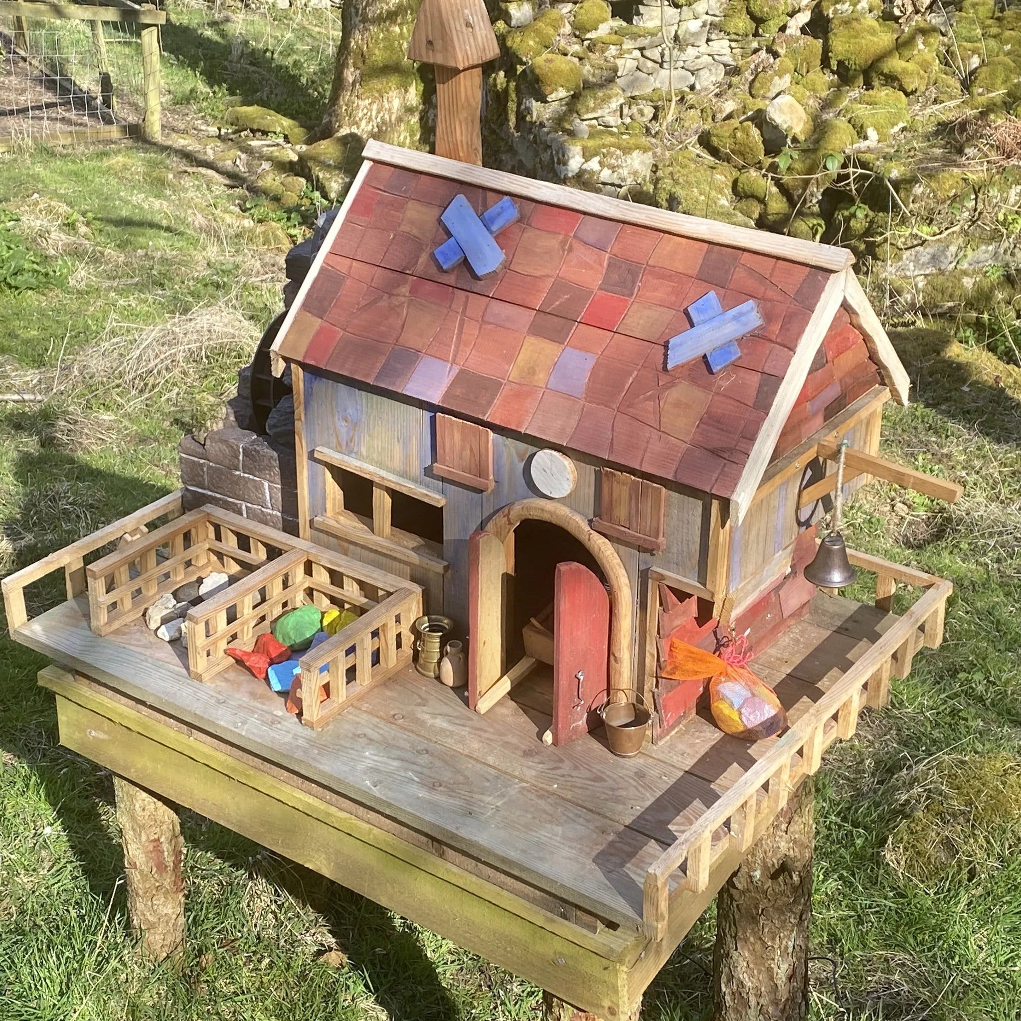 Handmade rustic wooden fairy cottage with stone-effect painted walls, arched windows and characterful tiny door