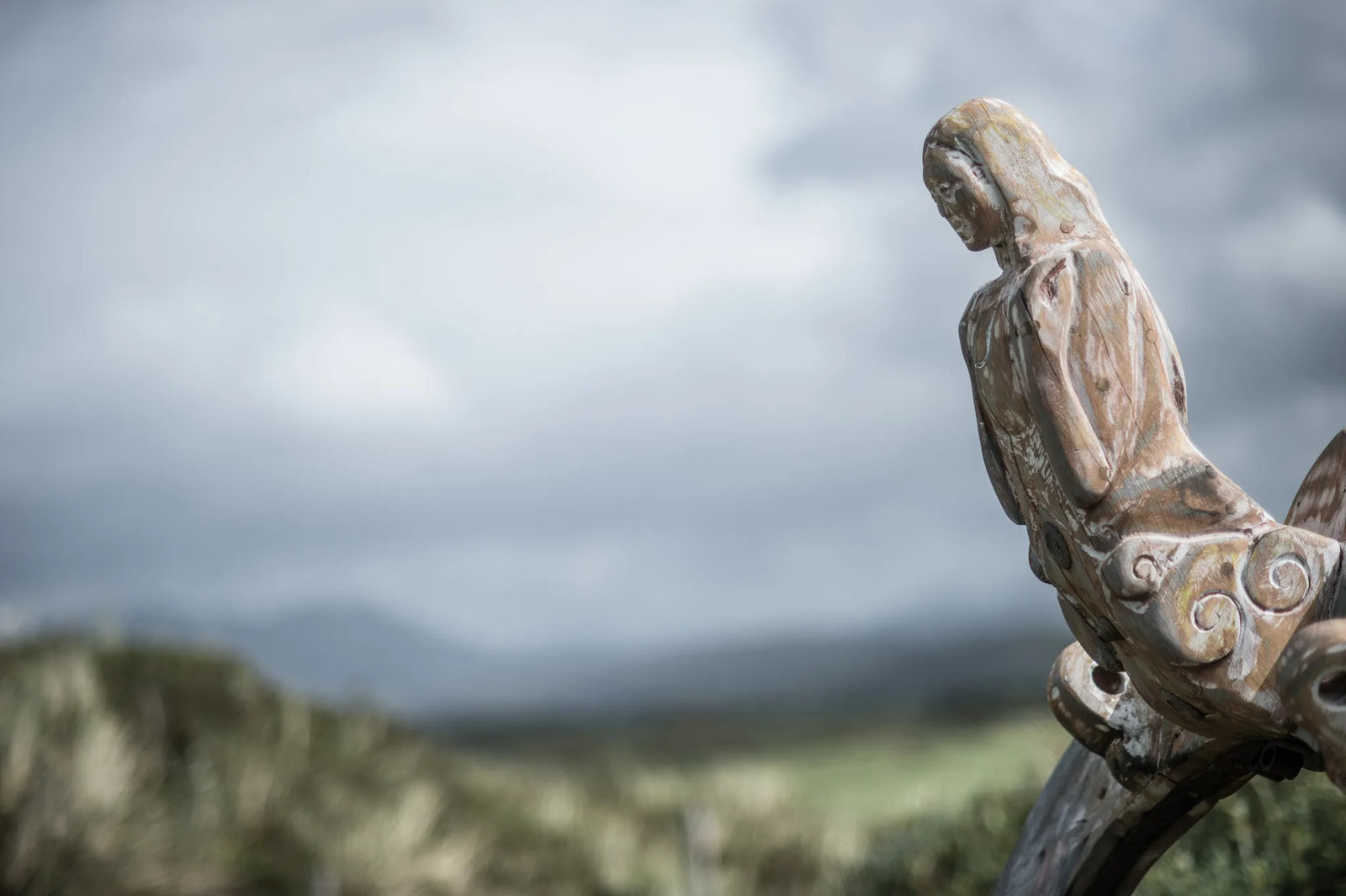 Close-up of hand-carved wooden figurehead on Shipwreck storytelling chair | oak mermaid figure against stormy sky