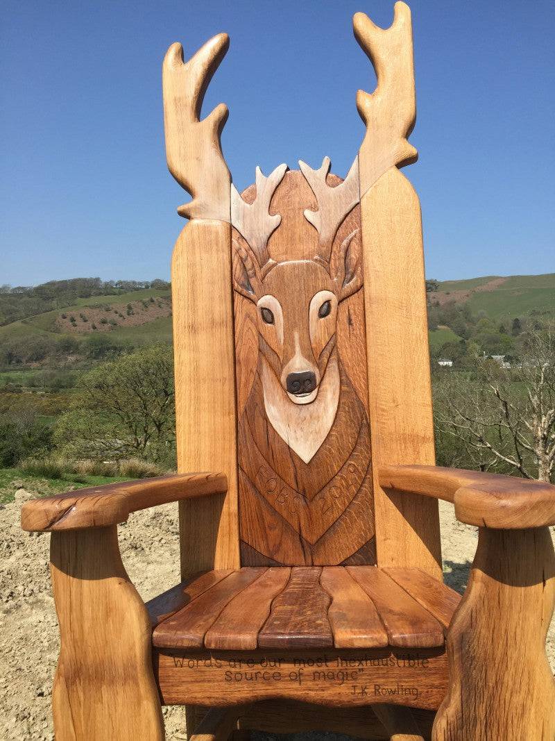 Solid oak stag storytelling chair in open landscape — handmade carved reading throne, Wales