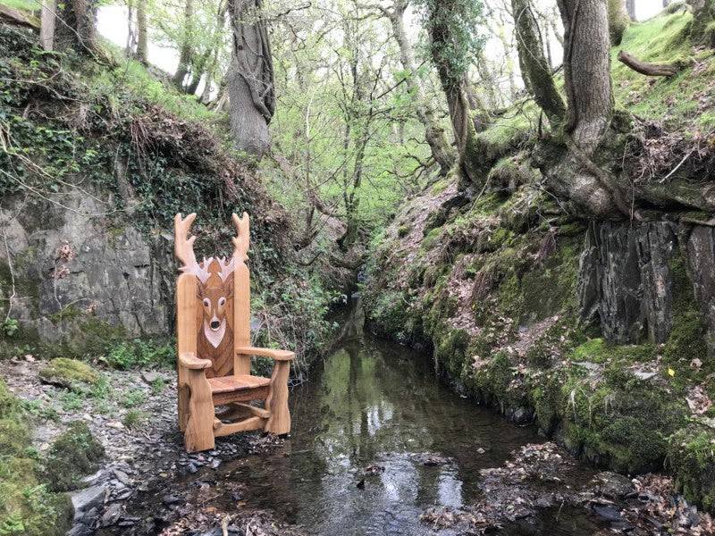 Handcrafted oak stag storytelling chair by woodland stream — bespoke carved reading throne, Wales