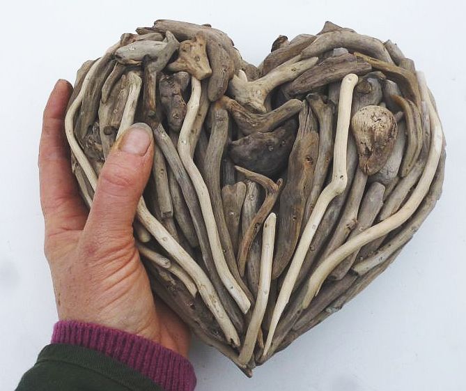 Hand hält kleine Herzskulptur aus Treibholz