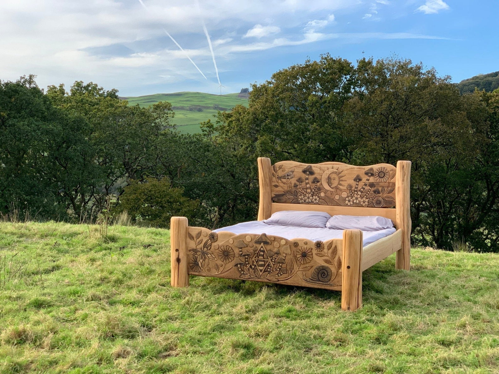 Bespoke oak fantasy bed with carved designs displayed outdoors — handmade in Mid Wales