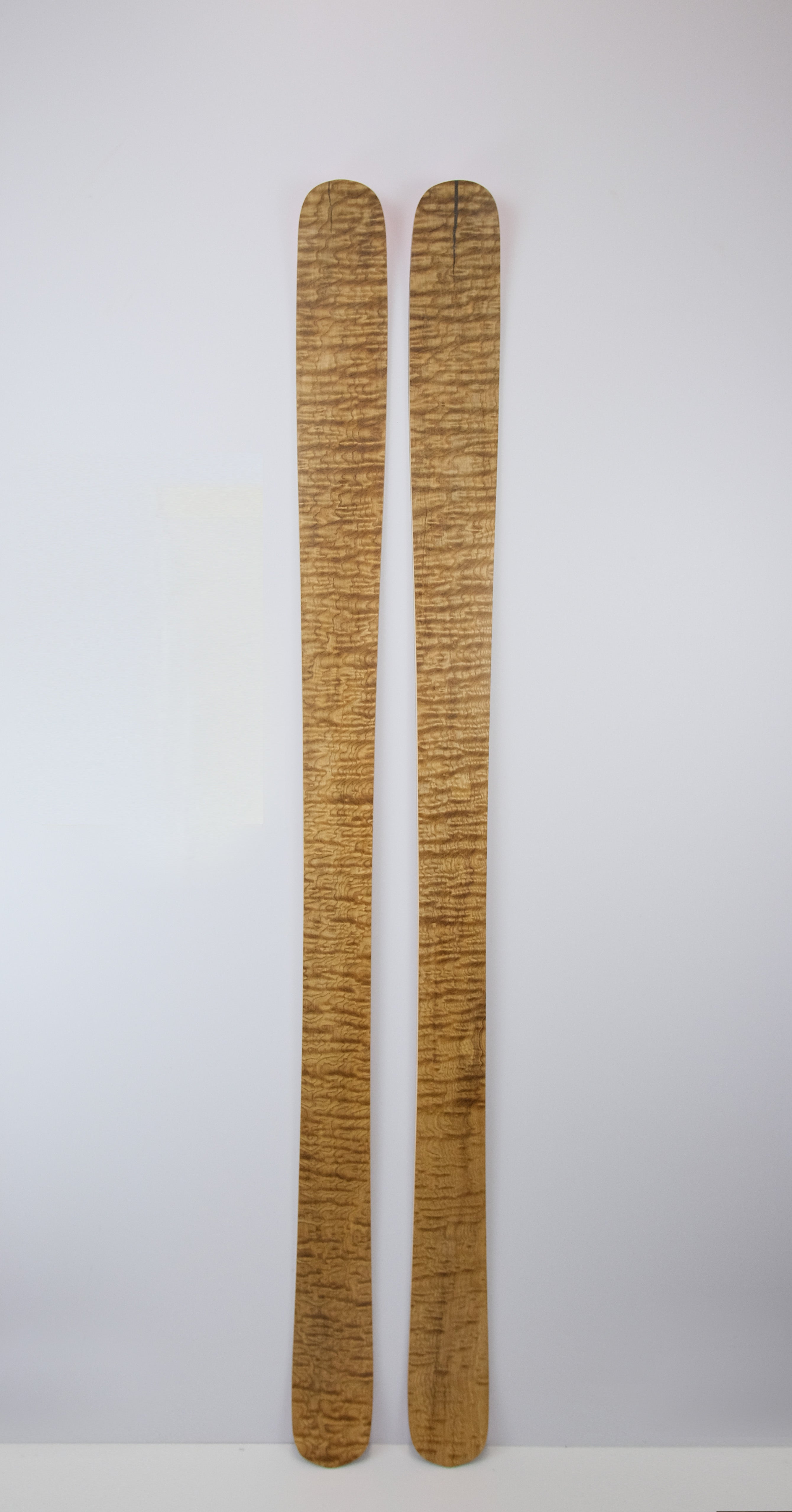 Front view of Twin Tip 98 skis showcasing the tan ash topsheet with a natural woodgrain texture, displayed upright against a white background