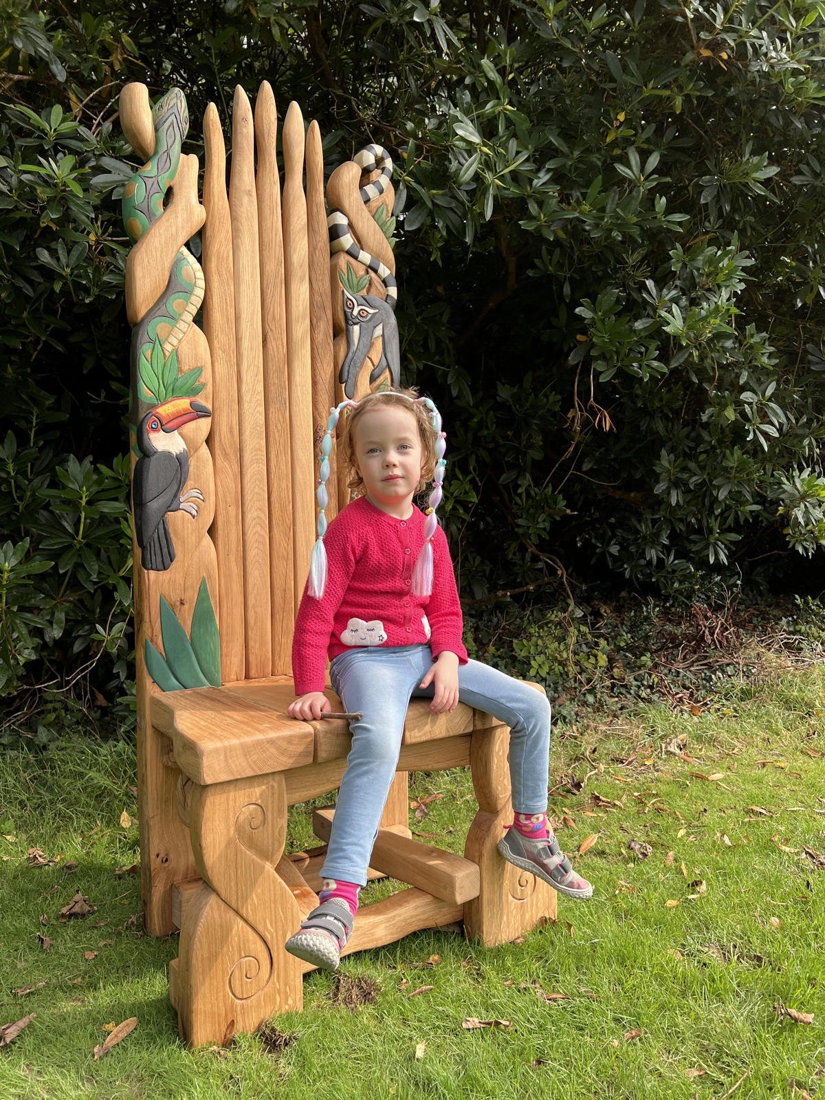 Child on jungle-inspired carved oak wildlife throne with toucan, jaguar and lemur — handmade, Wales