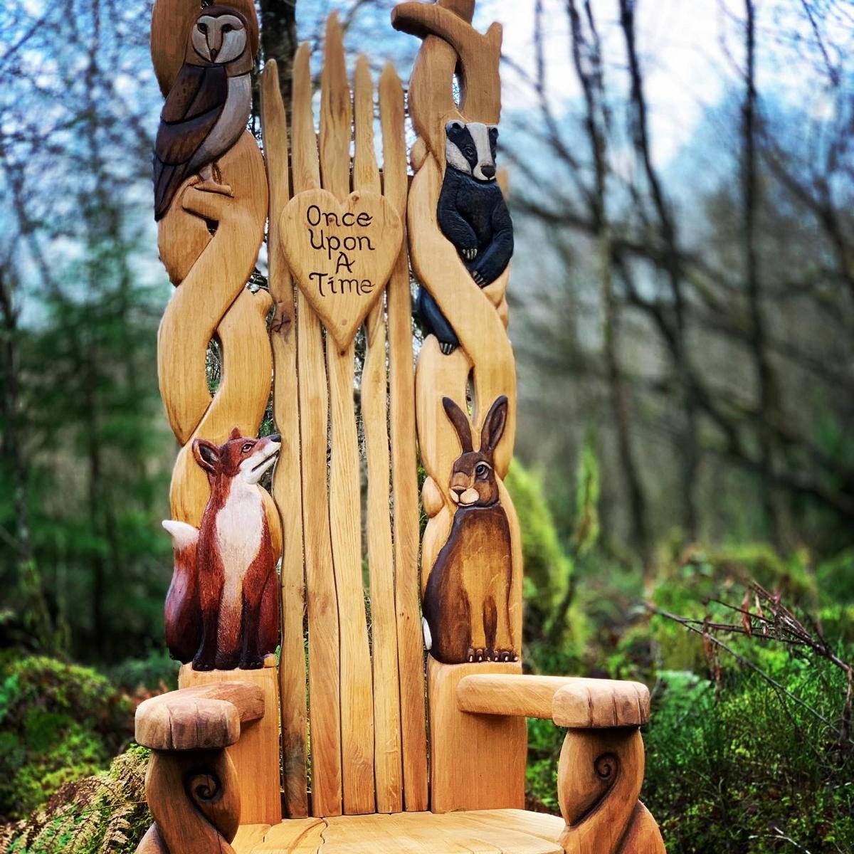 Backrest of Throne, a handcrafted oak storytelling chair featuring intricately carved woodland animals like foxes, owls, and badgers, set against a lush garden backdrop