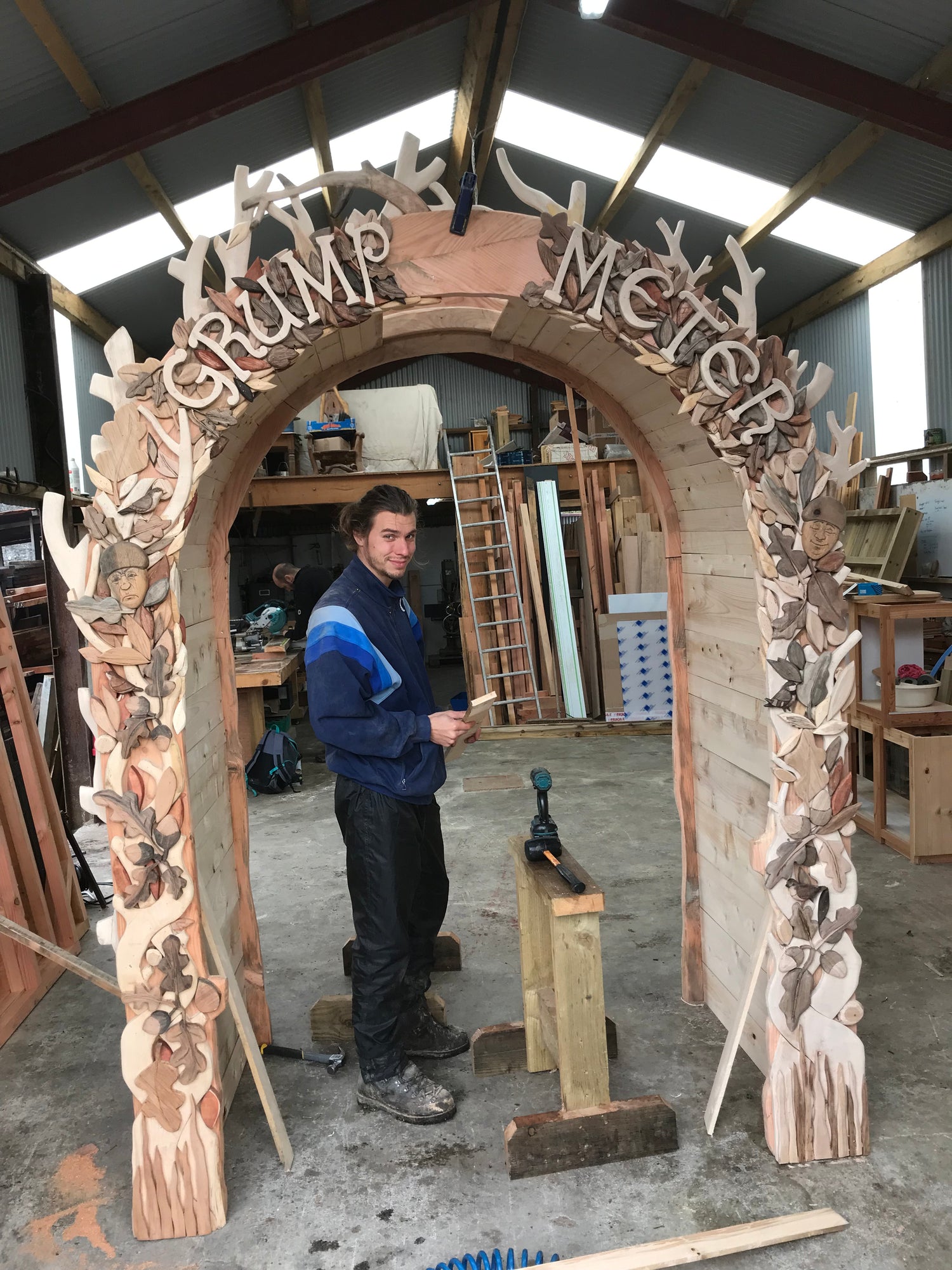 Arturo standing in a workshop next to a large wooden arch with 'GRUMP'S MEETER' text.
