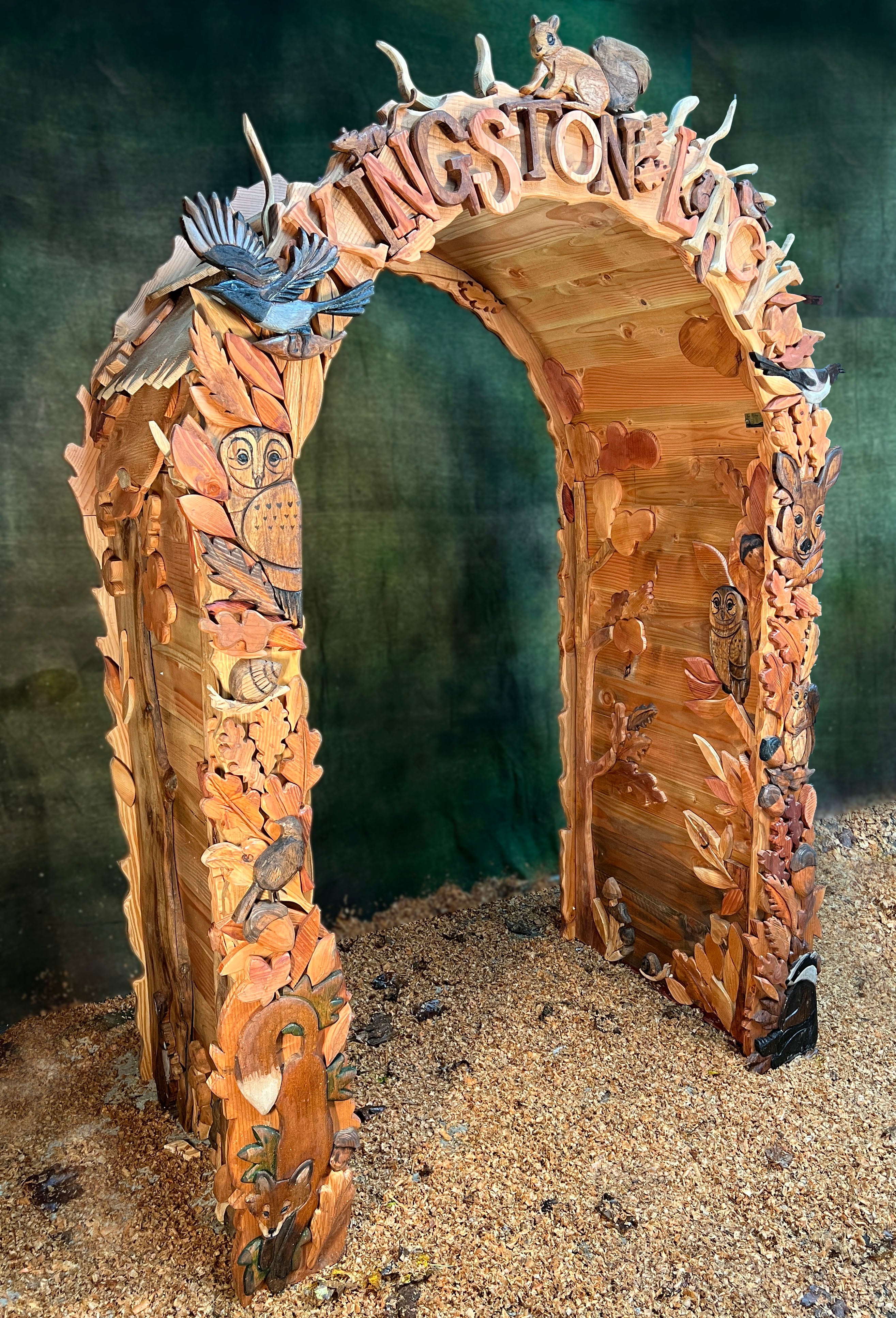 side angle of hand carved woodland arch featuring owl deer leaves and textured timber