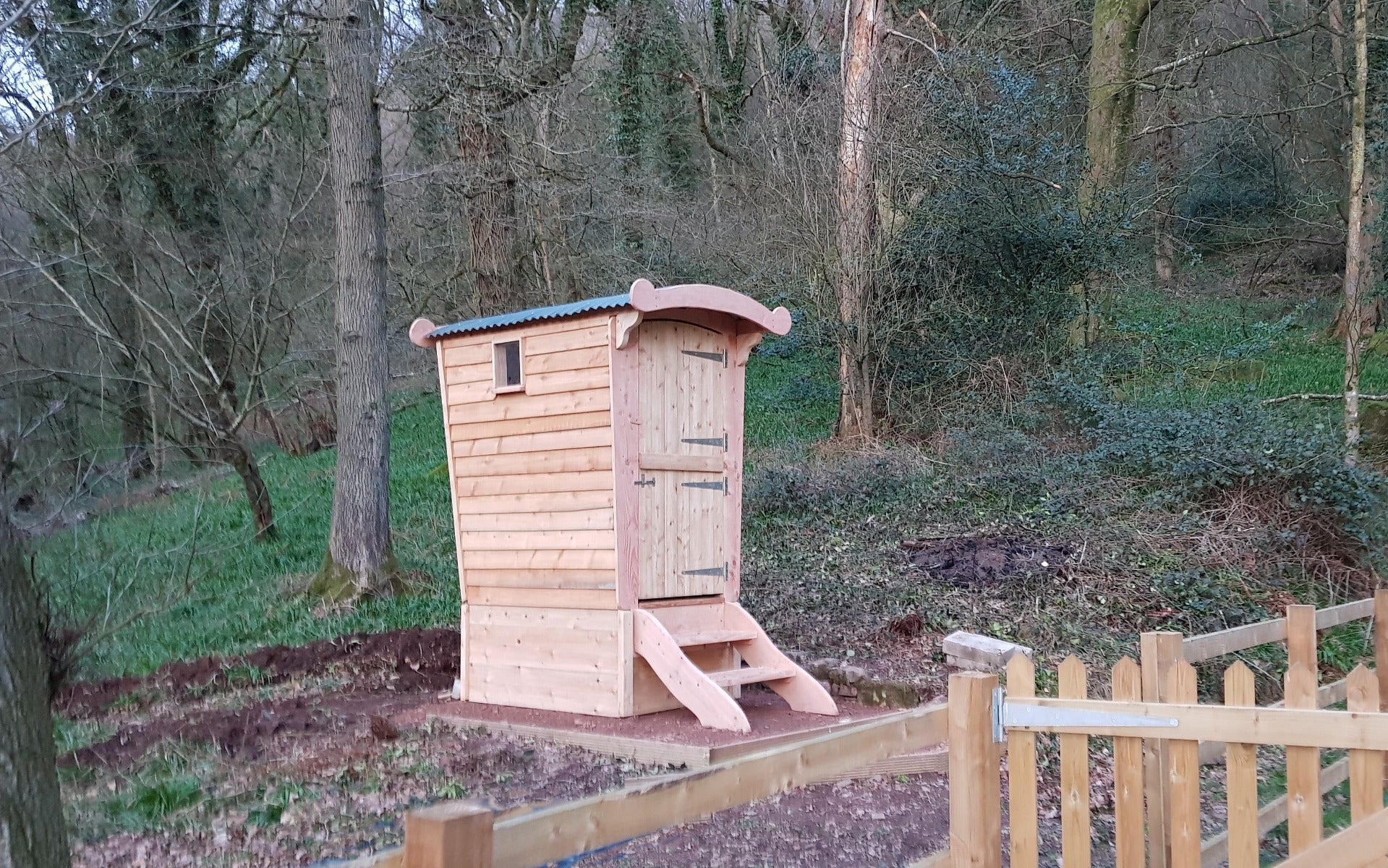 Compost toilet near wooden fence in forest