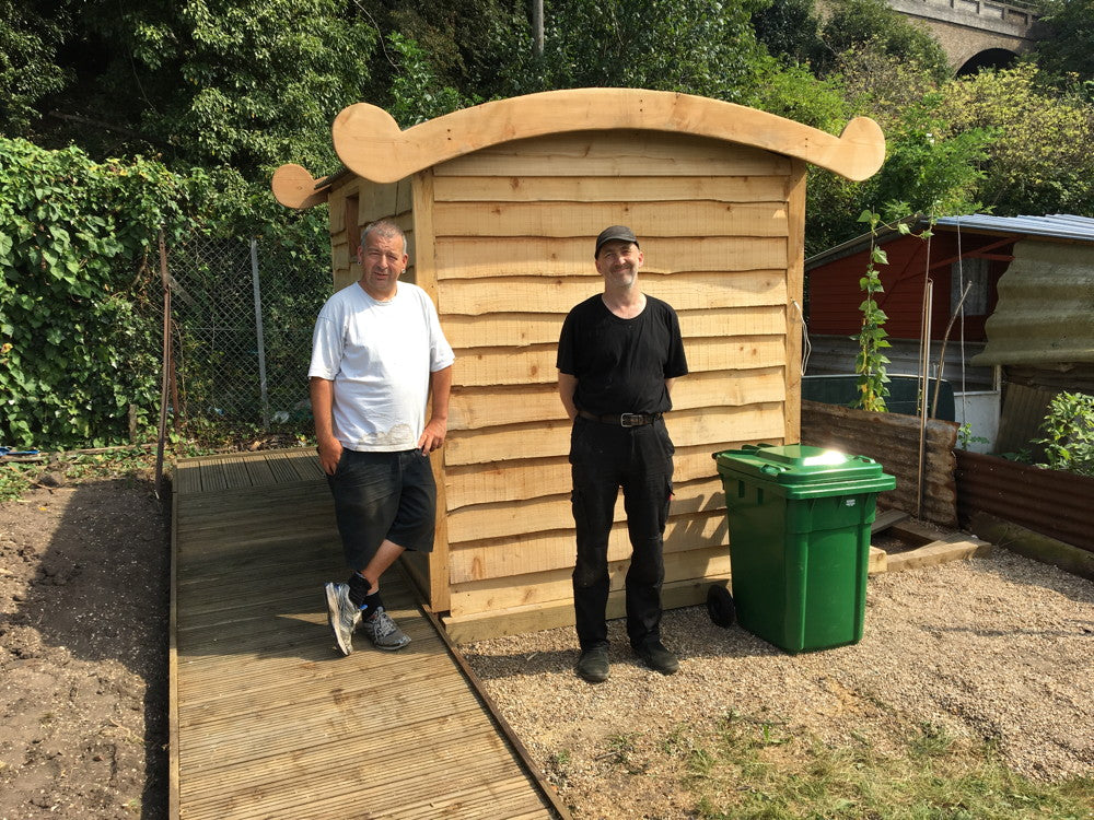 Two men beside a compost toilet with a green bin