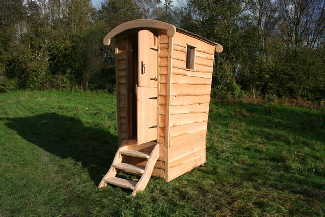 Wooden compost toilet on grassy landscape