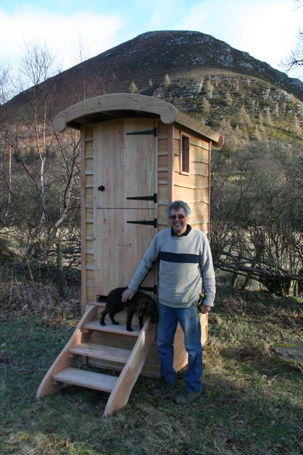 Man with dog beside wooden composting toilet outdoors