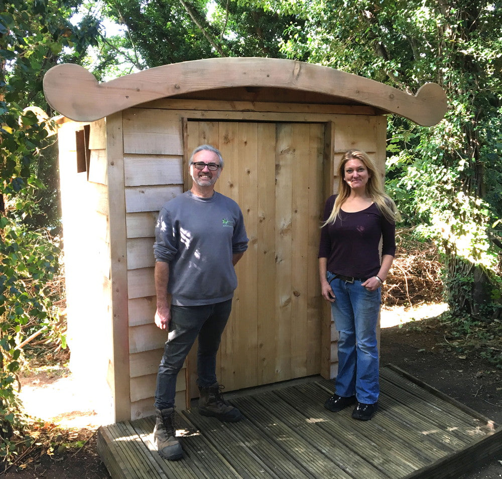 Two people standing in front of a wooden compost toilet