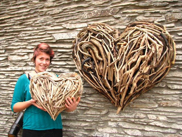 Person holding small driftwood heart next to large wall sculpture