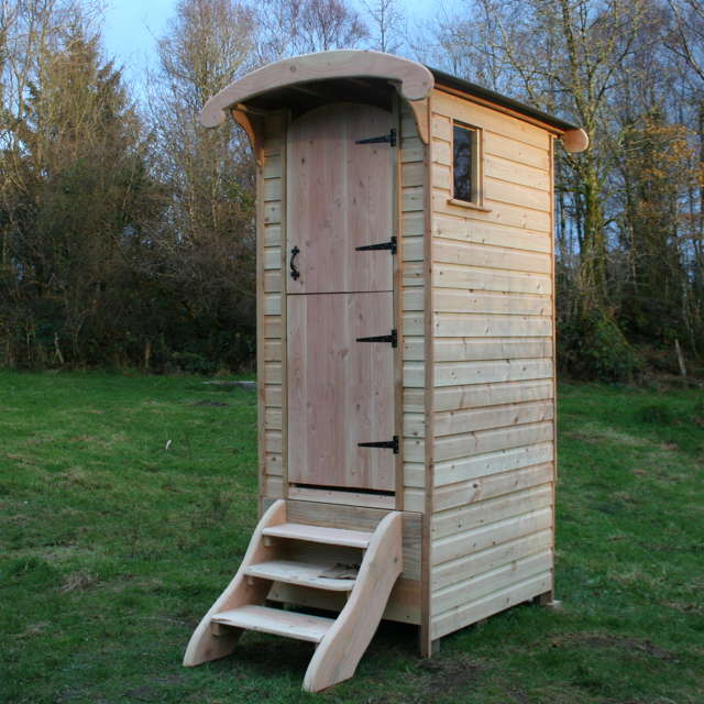 Wooden composting toilet with curved roof in field